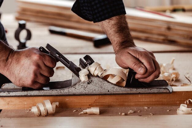 Tischlerhände, die eine Holzplanke mit einem Handhobel hobeln