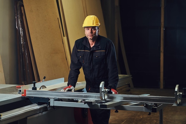 Tischlermann mit gelber sicherheitskappe arbeitet mit kettensäge in einer garage.