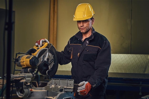 Kostenloses Foto tischlermann mit gelber sicherheitskappe arbeitet mit kettensäge in einer garage.