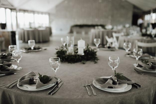Tischverpflegung mit grauen Servietten, Tischbesteck, Gabeln und Gläsern, dekoriert mit Grün und Kerzen