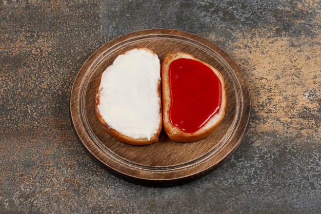 Toast mit Erdbeermarmelade und Sauerrahm auf Holzbrett.