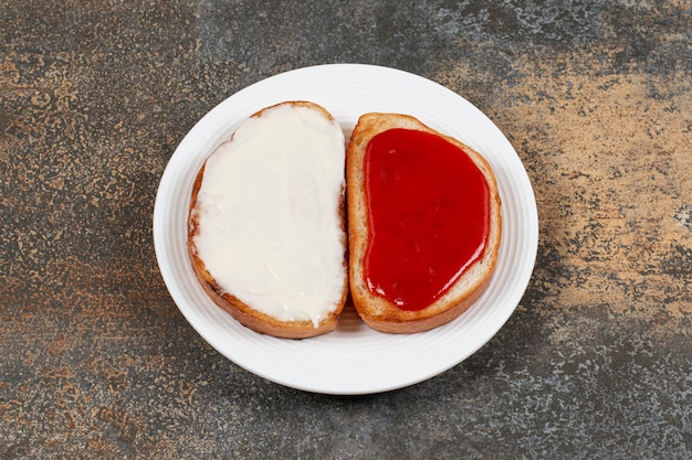 Toast mit Erdbeermarmelade und Sauerrahm auf weißem Teller.