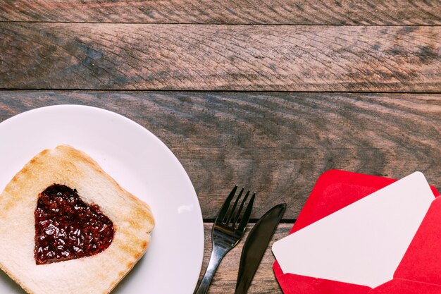 Toast mit Marmelade auf Teller in der Nähe von Umschlag und Besteck