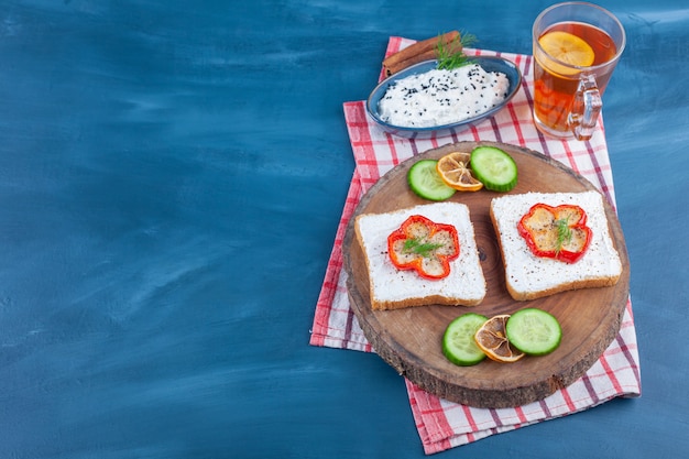 Toast mit sahne und paprika in scheiben auf holzstück und glas tee.