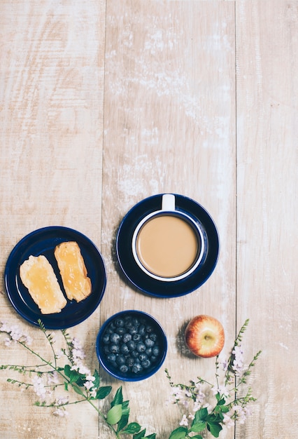 Toastbrot; Blaubeeren; Apfel und Tasse Kaffee auf hölzernen strukturierten Hintergrund