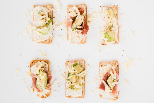 Toastbrot mit geriebenem Käse; Schinken-Avocado-Scheibe auf weißem Hintergrund