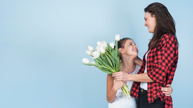 Tochter, die Mutter umarmt und ihren weißen Tulpen gibt