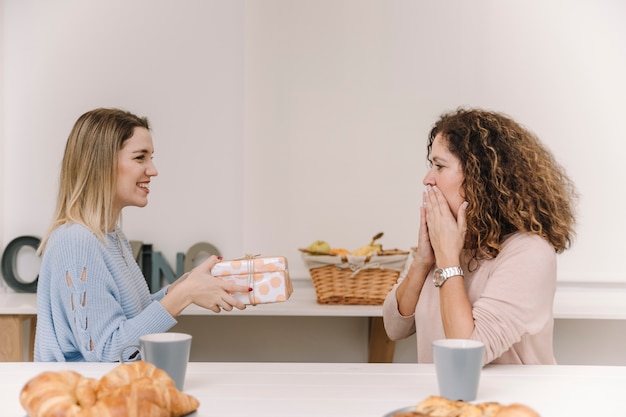 Tochter, die überraschter Mutter während des Frühstücks Geschenk gibt