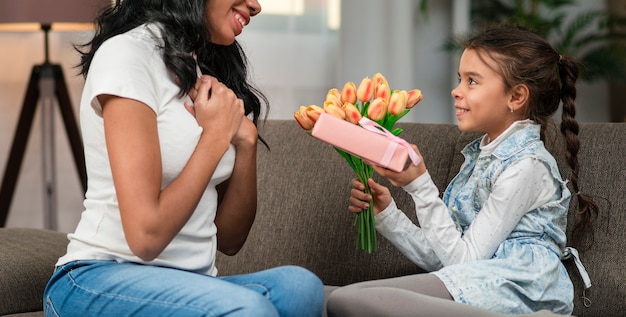 Tochter überrascht Mutter mit Blumen und Geschenk