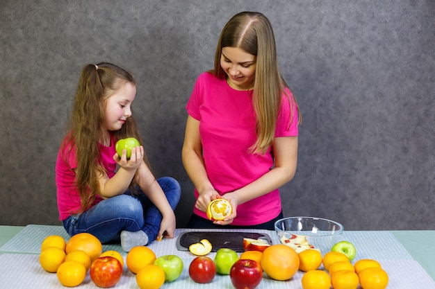 Tochter und mama schneiden einen obstsalat bestehend aus apfel-orange und mandarine