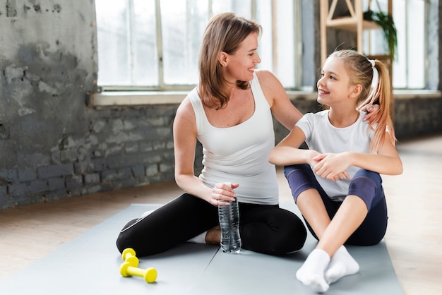 Tochter und Mutter auf Yogamatte schauen sich an