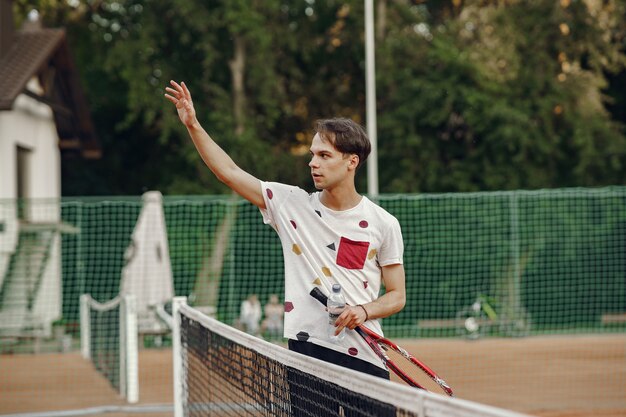 Toller Tag zum Spielen! Fröhlicher junger Mann im T-Shirt. Kerl hält Tennisschläger und Ball.