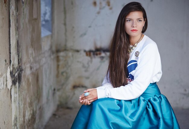 Tolles Mädchen mit langen Haaren und langem blauem Kleid, das vor der Kamera posiert.