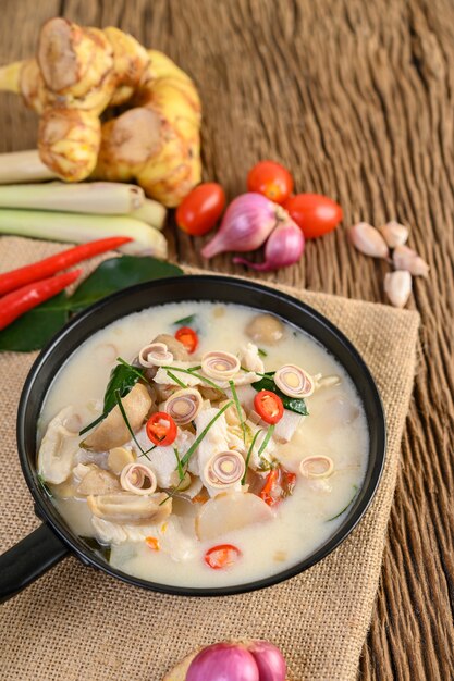 Tom Kha Kai in einer Pfanne mit Kaffirlimettenblättern, Zitronengras, roten Zwiebeln, Galangal und Chili.