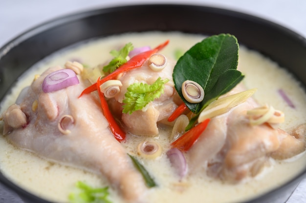 Tom Kha Kai in einer Pfanne mit Kaffirlimettenblättern, Zitronengras, roten Zwiebeln, Galangal und Chili.