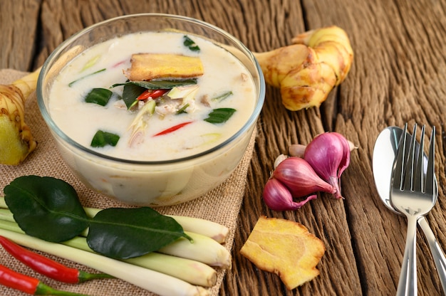 Tom Kha Kai in einer Schüssel mit Kaffirlimettenblättern, Zitronengras, roten Zwiebeln, Galangal und Chili.