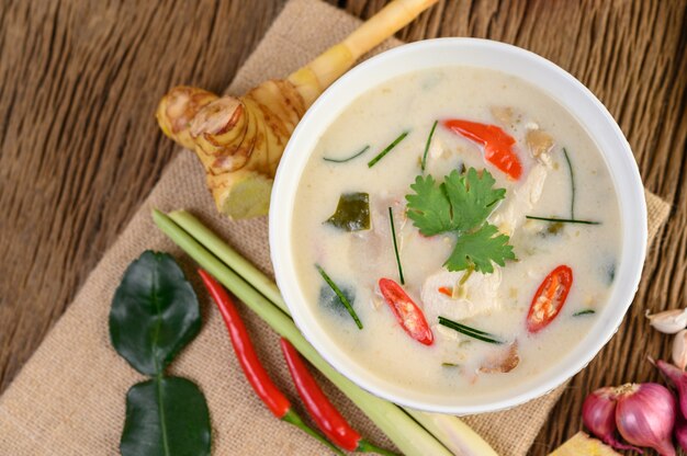 Tom Kha Kai in einer Schüssel mit Kaffirlimettenblättern, Zitronengras, roten Zwiebeln, Galangal und Chili.