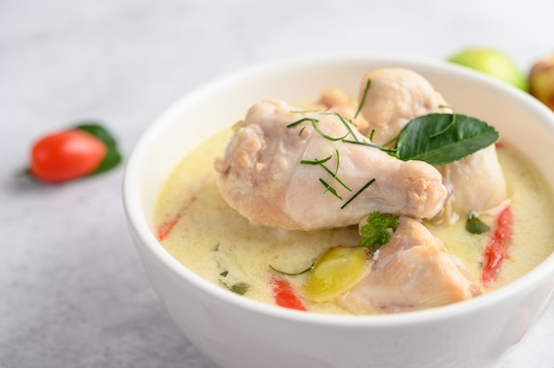 Tom Kha Kai in einer Schüssel mit Kaffirlimettenblättern, Zitronengras, roten Zwiebeln, Galangal und Chili.