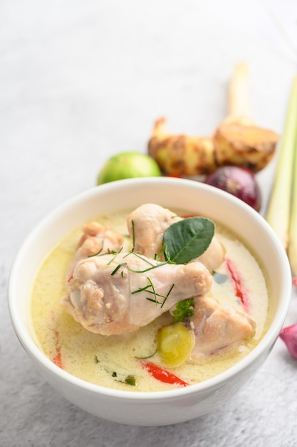 Tom Kha Kai in einer Schüssel mit Kaffirlimettenblättern, Zitronengras, roten Zwiebeln, Galangal und Chili.