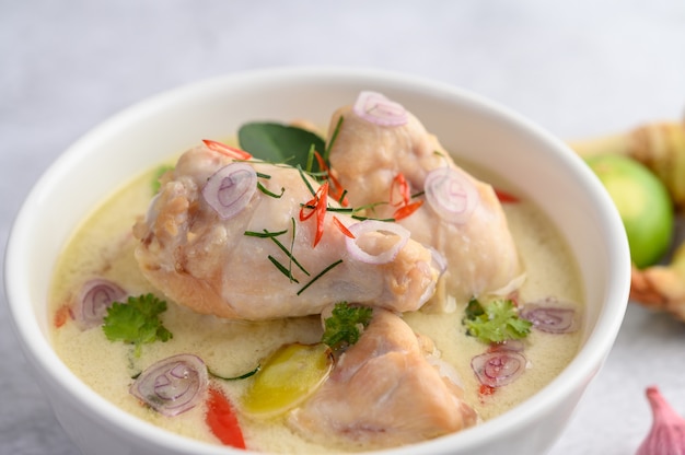 Tom Kha Kai in einer Schüssel mit Kaffirlimettenblättern, Zitronengras, roten Zwiebeln, Galangal und Chili.