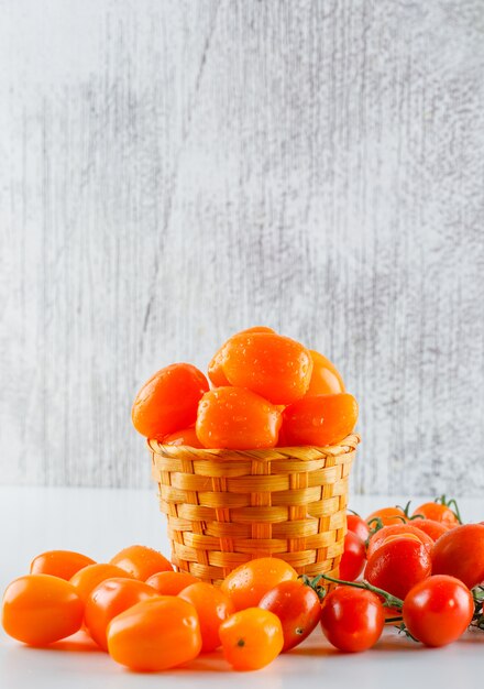 Tomaten in einem Weidenkorb auf weißem und schmuddeligem Tisch. Seitenansicht.