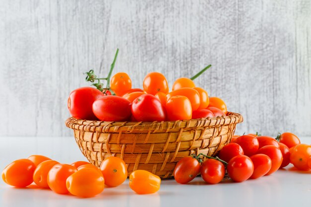 Tomaten in einem Weidenkorb auf weißem und schmuddeligem Tisch. Seitenansicht.