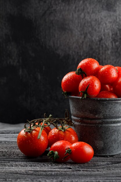 Tomaten in einer Mini-Eimerseitenansicht auf grauer hölzerner und dunkler Wand