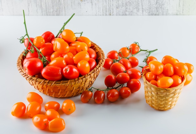 Tomaten in Weidenkörben auf weißem und schmuddeligem Tisch, hohe Winkelansicht.