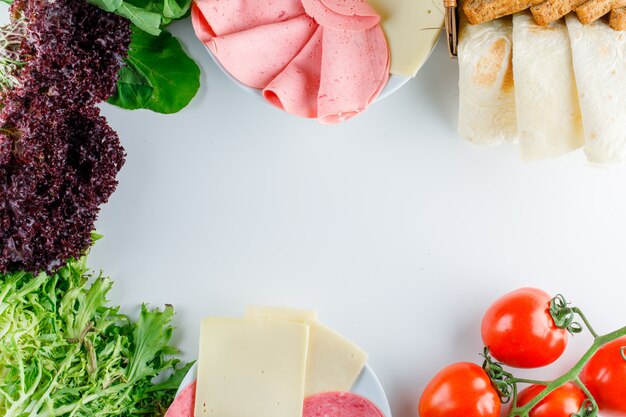 Tomaten mit Blattgemüse, rotem Salat, Brot, Käse, Wurst, flach gelegt.