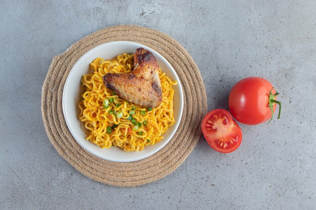 Tomaten und Nudelschale auf einem Untersetzer, auf dem Marmorhintergrund.