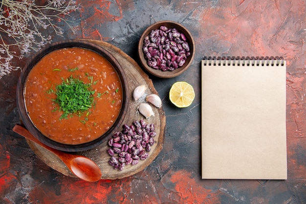 Tomatensuppe Bohnen Knoblauch auf Holz Schneidebrett Löffel und Notizbuch auf Mix Farbtabelle