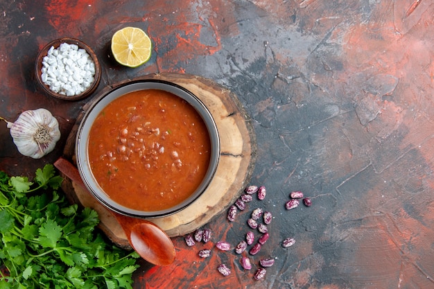 Tomatensuppe in einem blauen Schüssellöffel auf Holztablett Knoblauchsalz und Zitrone ein Bündel Grün auf gemischten Farbtabellenaufnahmen