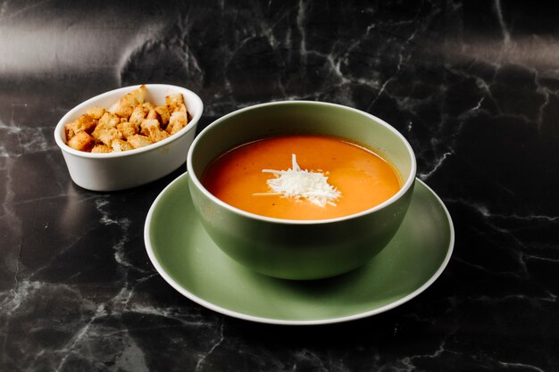 Tomatensuppe innerhalb der grünen Schüssel mit gehacktem Weißkäse auf ihr mit Crackerschüssel herum.