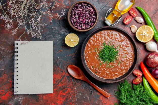 Tomatensuppe Ölflasche Bohnen Zitrone ein Bündel Grün und Notizbuch auf gemischten Farbtabellen