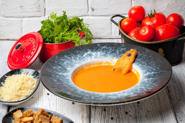 Tomatensuppe von der Seite mit frischen Tomaten, Gemüse und Käse auf dem Tisch