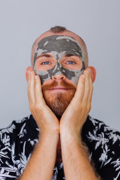 Tonmaske auf Gesicht des jungen gutaussehenden Mannes in der Schönheitsklinik