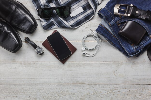 Top-Ansicht-Accessoires, um mit Mann-Kleidung-Konzept zu reisen. Hemd, Baumwollstoff, Handy auf hölzernem background.watch, Sonnenbrille und Schuhe auf hölzerner Tabelle.