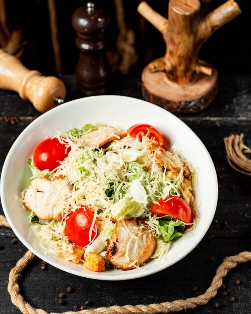 Top Caesar Salat mit Huhn und Parmesan in der Schüssel auf dunkel