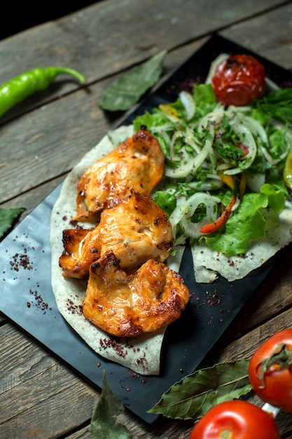 Top Chicken Kebab serviert mit Zwiebeln frische Kräuter gegrillte Tomaten und Pfeffer auf schwarzem Brett