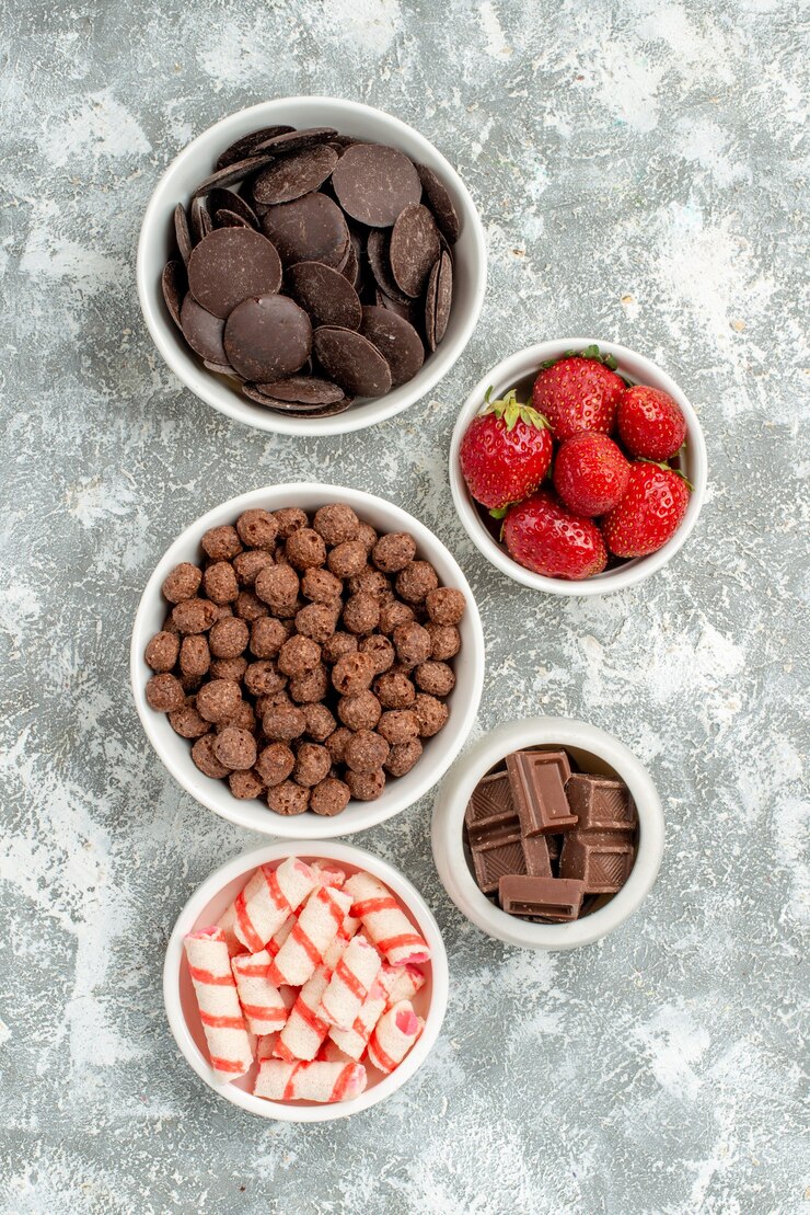 Kostenlose Foto top close view schalen mit süßigkeiten erdbeeren pralinen müsli und kakao auf dem grau-weißen boden mit freiem platz