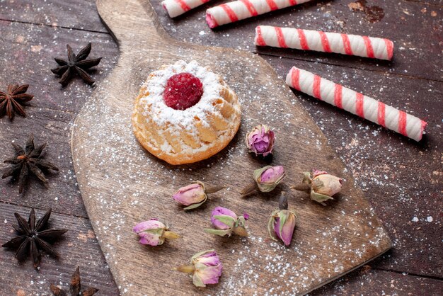 Top entfernte Ansicht des kleinen cremigen Kuchens mit Himbeere zusammen mit rosa Stockbonbons auf braunem hölzernem, süßem Zuckerkuchen des Bonbons