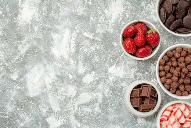 Top Fernsichtschalen mit Süßigkeiten Erdbeeren bitter und milchig Pralinen Müsli und Kakao auf der rechten Seite des grauweißen Bodens