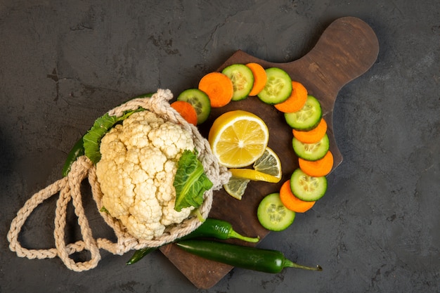 Top Karotten- und Gurkenscheiben und Blumenkohl auf Holzschneidebrett im Dunkeln