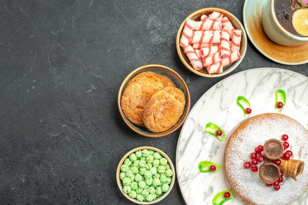 Top Nahaufnahme Ansicht Süßigkeiten Kuchen mit roten Johannisbeeren bunte Süßigkeiten Waffeln Kekse eine Tasse Tee mit Zitrone