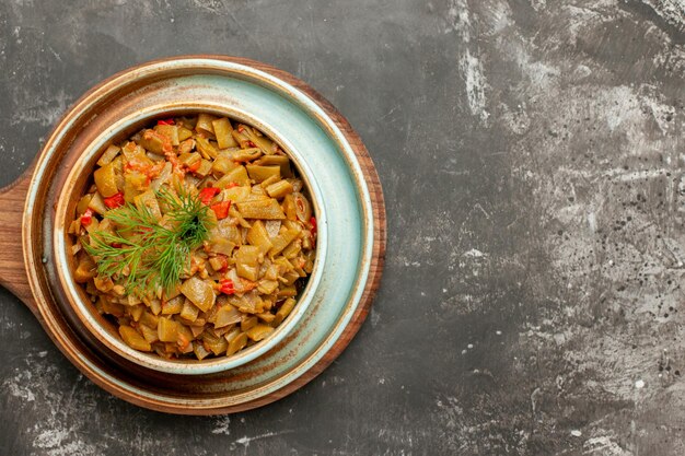 Top Nahaufnahme appetitanregendes Gericht grüne Bohnen mit Tomaten auf dem Holztablett auf dem Schneidebrett auf dem dunklen Tisch