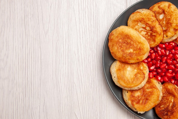 Top Nahaufnahme appetitliche Pfannkuchen appetitliche Pfannkuchen mit Granatapfelkernen auf dem Teller auf dem weißen Tisch