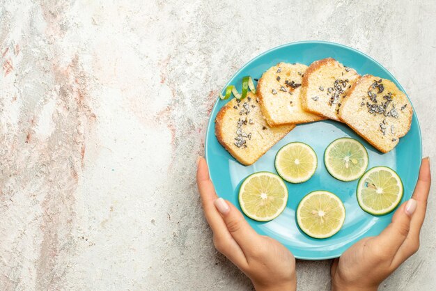 Top Nahaufnahme Brot und Zitrone blaue Platte Brot und geschnittene Zitrone in der Hand auf dem weißen Tisch