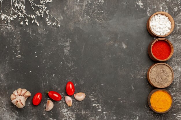 Top Nahaufnahme bunte Gewürze vier Schüsseln mit bunten Gewürzen Knoblauch und Tomaten neben den Ästen auf dem schwarzen Tisch