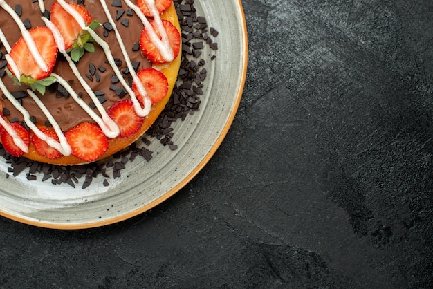 Top Nahaufnahme Dessert appetitlicher Kuchen mit Schokoladen- und Erdbeerstücken auf weißem Teller auf der linken Seite des dunklen Tisches