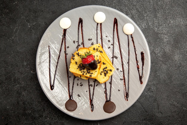 Top nahaufnahme dessert kuchenstücke mit schokoladenüberzogenen erdbeeren und schokoladensauce auf dem grauen teller auf dem dunklen tisch Kostenlose Fotos